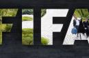 FILE - In this May 27, 2015, file photo, two persons are reflected in the FIFA logo at the FIFA headquarters in Zurich, Switzerland. Swiss authorities said Thursday, July 16, 2015, that one of the seven FIFA officials arrested in Zurich as part of a U.S. corruption probe was extradited to the United States they day before. Switzerland's Federal Office of Justice didn't identify the FIFA official. (AP Photo/Michael Probst, File)