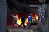 People run past a burning car after loyalist protesters attacked the police with bricks and bottles as they waited for a republican parade to make it's way through Belfast City Centre, August 9, 2013. REUTERS/Cathal McNaughton