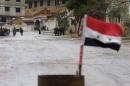 A Syrian national flag flutters near residents who said they have received permission from the Syrian government to leave the besieged town as they wait with their belongings after an aid convoy entered Madaya, Syria