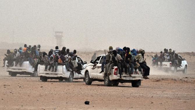 Migrants sit on pick-up trucks, holding wooden sticks tied to the vehicle to avoid falling from it, as they leave the outskirts of Agadez for Libya, from where they will try to reach Europe, on June 1, 2015