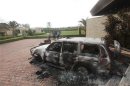 People stand near a burnt car at the U.S. consulate, which was attacked and set on fire by gunmen yesterday, in Benghazi