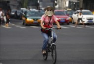 Una mujer con la cara cubierta con una máscara pedalea por las calles de Pekín, China. EFE/Archivo