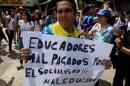 In this Thursday, May 28, 2015 photo, a teacher holds a poster that reads in Spanish " Teachers underpaid by rude socialism" during a protest in Venezuela's Central University, UCV, in Caracas, Venezuela. College professors in this socialist country plagued by a cash crunch, shortages and spiraling inflation are abandoning their jobs in droves, unable or unwilling to survive on salaries as minuscule as $30 per month. (AP Photo/Fernando Llano)