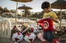 A boy holds a Tunisian flag as he stands near bouquets of flowers laid at the beachside of the Imperiale Marhabada hotel, which was attacked by a gunman in Sousse