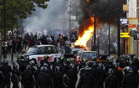 REUTERS/Luke MacGregor - Police officers in riot gear block a road near a burning car on a London street.