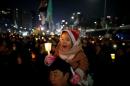 A child sitting on his father's shoulder holds a candlelight during a protest demanding South Korean President Park Geun-hye's resignation in Seoul