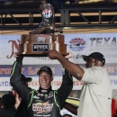 With the help of former professional basketball player Karl Malone, right, Sprint Cup Series's Kyle Busch (18) raises the trophy after winning the NASCAR Sprint Cup series NRA 500 auto race at Texas Motor Speedway  Saturday, April 13, 2013, in Fort Worth, Texas. (AP Photo/Tony Gutierrez)