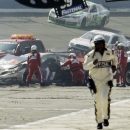 Rescue workers tend to the wreckage of the No. 11 FedEx Express Toyota driven by Denny Hamlin after he collided with Joey Logano on the final lap of the NASCAR Sprint Cup series auto race in Fontana, Calif., Sunday March 24, 2013. The pair had been battling for the lead the last three laps.  The No. 18 car of Kyle Busch passes behind on its vicory lap. (AP Photo/Reed Saxon)