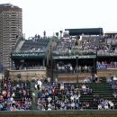 In this May 17, 2013 photo, spectators watch a Chicago Cubs baseball game from several of the rooftop bleachers across the field from Wrigley Field in Chicago. A battle is heating up between the Cubs and rooftop owners across the street from the ballpark as the team proposes renovations, including a Jumbotron in the bleachers, that would block the views and threaten the business those views have created. (AP Photo/Charles Rex Arbogast)